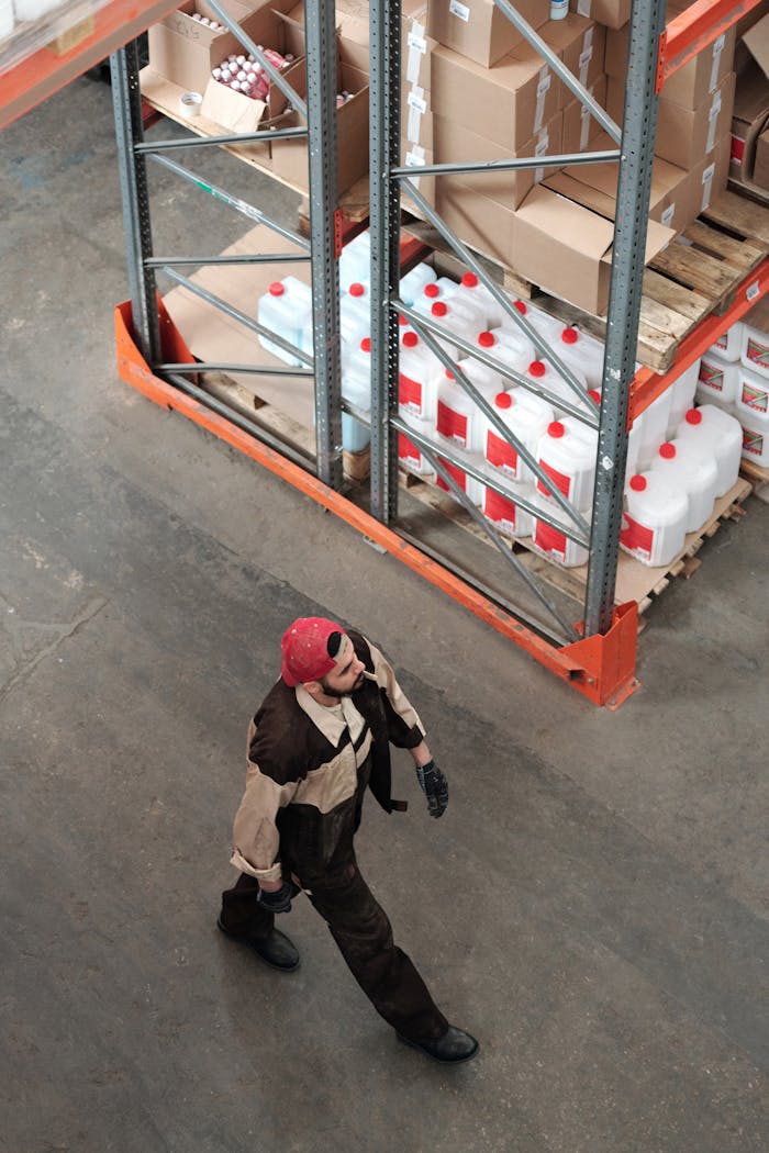 Crafting Captivating Headlines: Your awesome post title goes here Warehouse worker walking among shelves stocked with packages and containers, captured from a high angle.